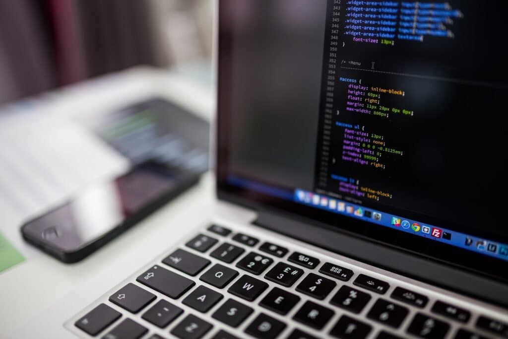 A laptop showing source code in an editor, with a smartphone on the desk beside it