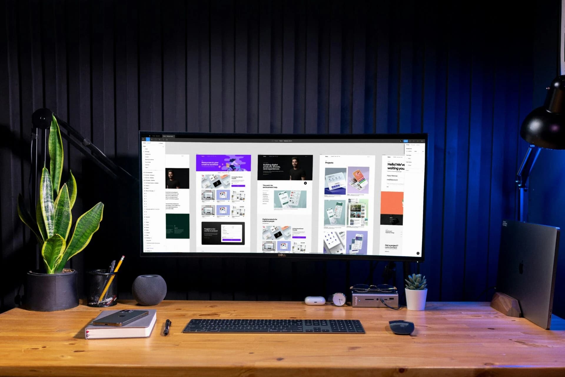 Ultrawide monitor showing app and web interface designs on a wooden desk