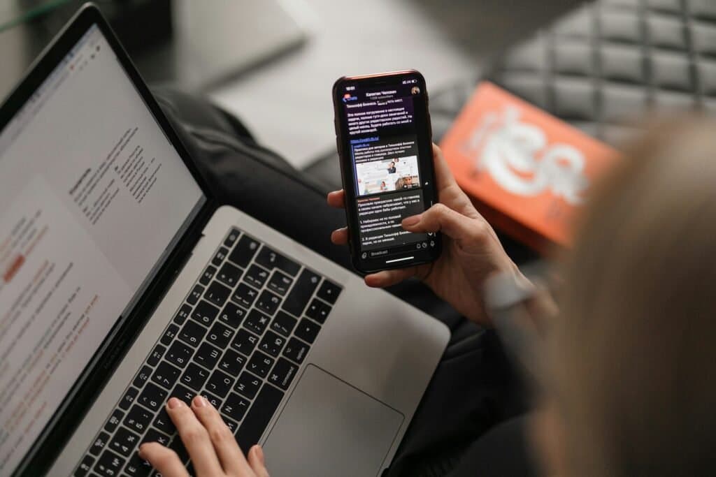 A person holding a smartphone with a message open while working on a laptop