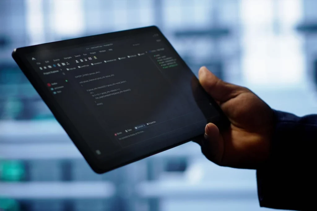 Hand holding a tablet showing code, representing DevOps monitoring and deployment by Aaga